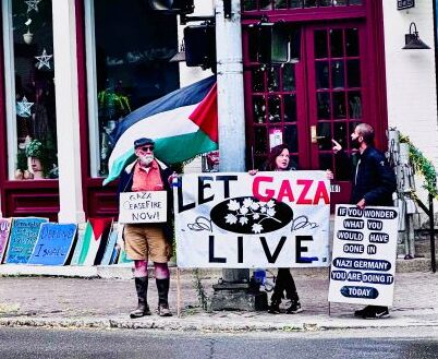 Demonstrators with signs and a Palistinian Flag by road