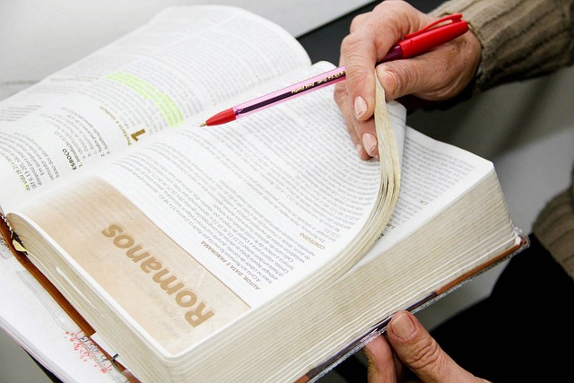 Image of bible with a hand holding pen, studying it.