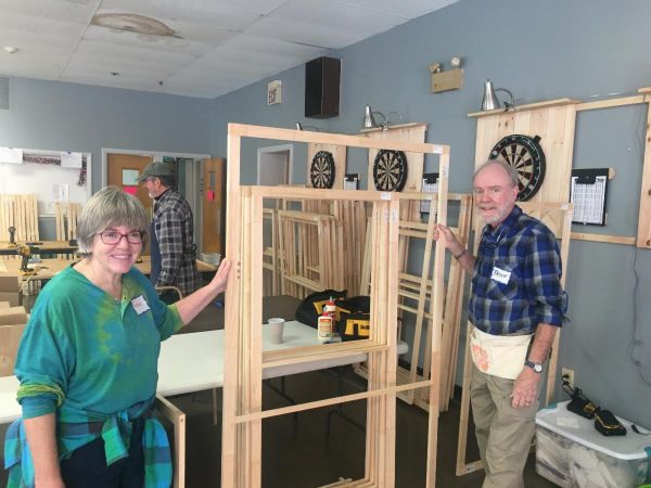 Man and woman with tool belts holding up a wooden window frame